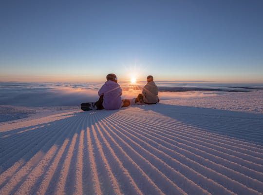 Två personer sitter i skidbacken och kollar på solnedgången.