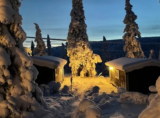 Bilden visar två snötäckta stugor i Sälen som är upplysta i ett mysigt gult lampskimmer.