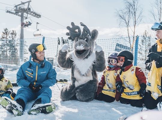 Bilden visar Idre Fjälls maskot Aske som sitter i en ring med en skidskolelärare och några barn.