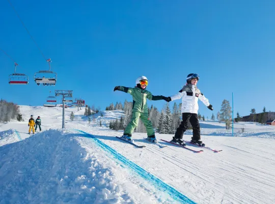 Bilden föreställer två glada barn på skidor som håller handen
